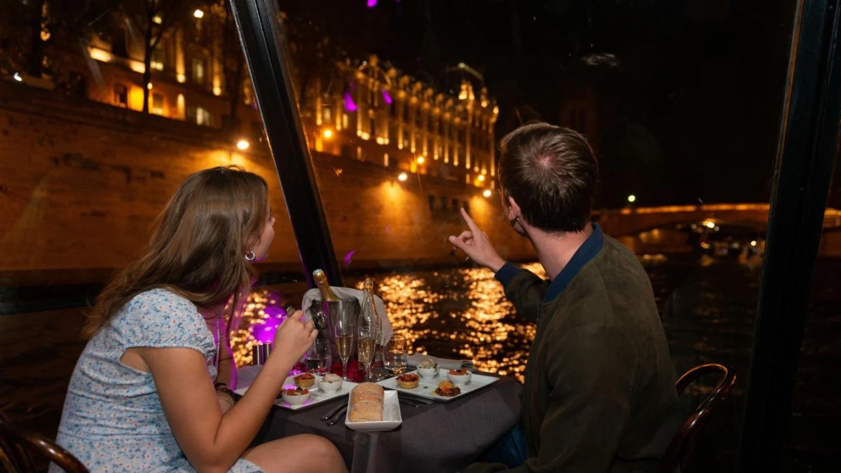 A couple having dinner on Seine River cruise watching lighted landmarks nearby. A couple having dinner on Seine River cruise watching lighted landmarks nearby.