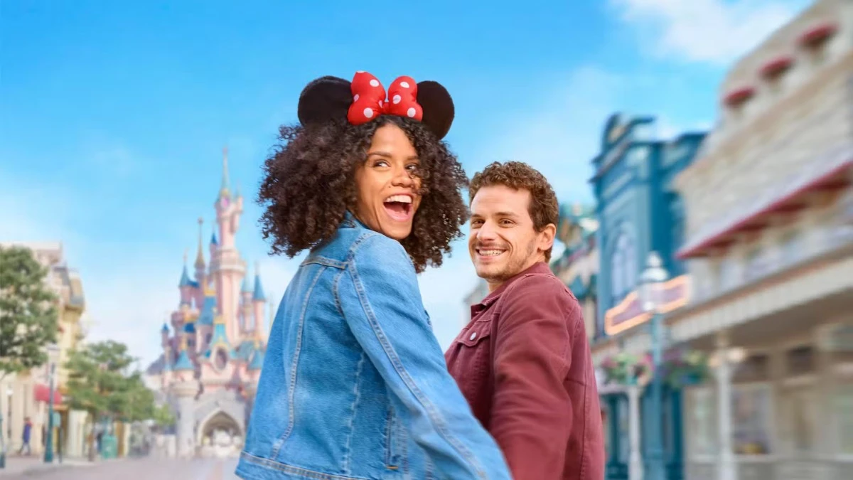 A happy couple, with the woman wearing Minnie Mouse ears, looking back at the camera with a Disney castle in the background.