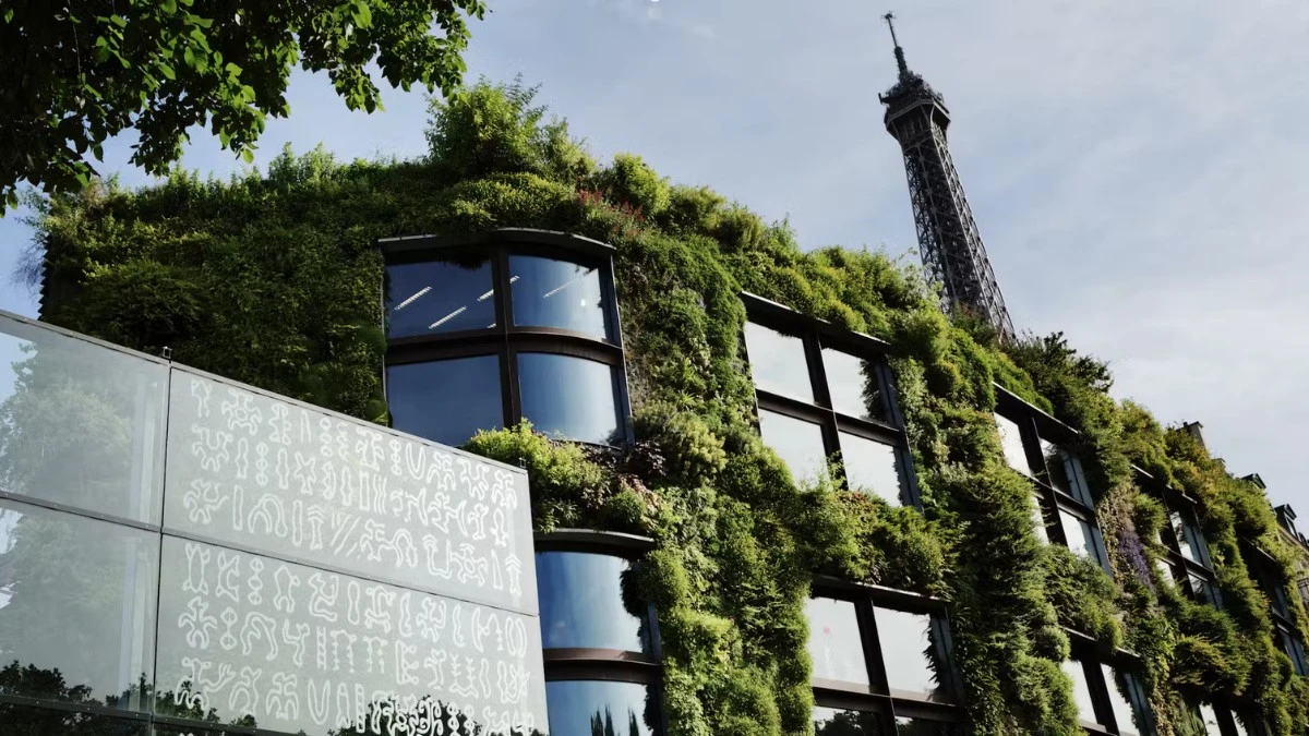 A building covered in green foliage with the top of the Eiffel Tower visible in the background.
