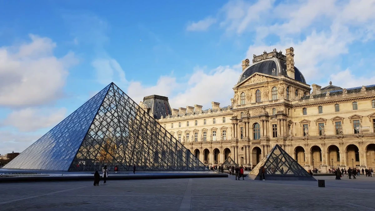 Louvre Pyramid and museum building on a clear day with people around.