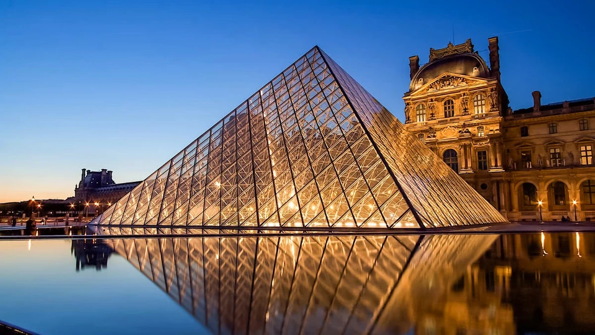 The illuminated Louvre Pyramid reflected in water at dusk.