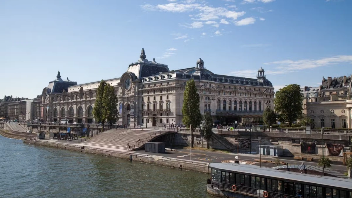 The exterior of the Musée d'Orsay building along the Seine River, with a tour boat docked nearby.