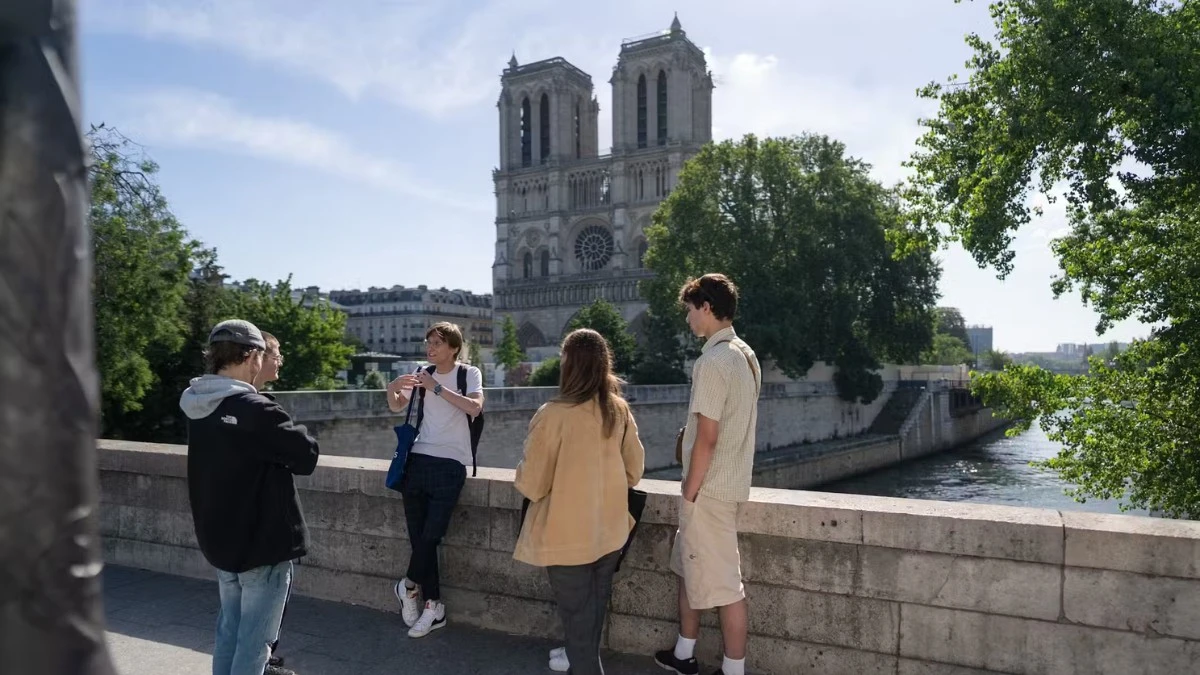 A group of students standing on a bridge, looking towards Notre Dame Cathedral.