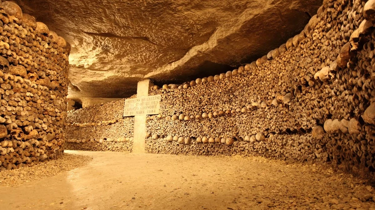 An underground passage in the Paris Catacombs lined with stacks of human skulls and bones.