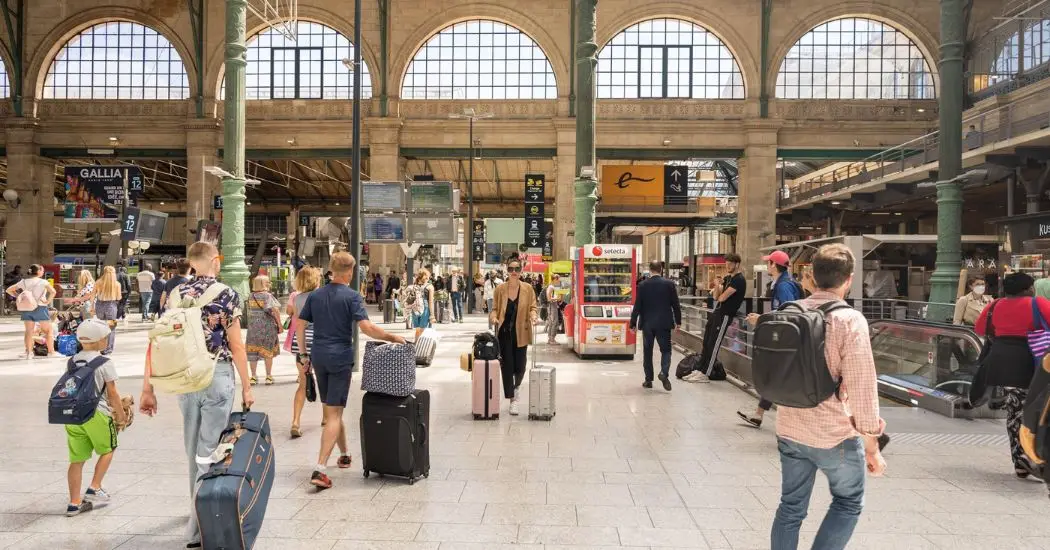 Crowds at Paris railway station with suitcases and information screens.