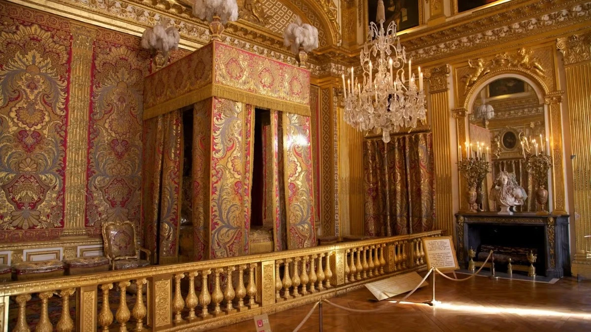 The ornate King's Bedchamber in the Palace of Versailles, featuring a grand bed, golden furnishings, and a chandelier.