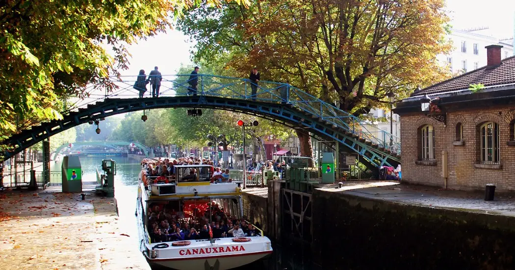 A sightseeing boat on the Canal Saint-Martin in Paris enters a lock under a romantic footbridge. A sightseeing boat on the Canal Saint-Martin in Paris enters a lock under a romantic footbridge.