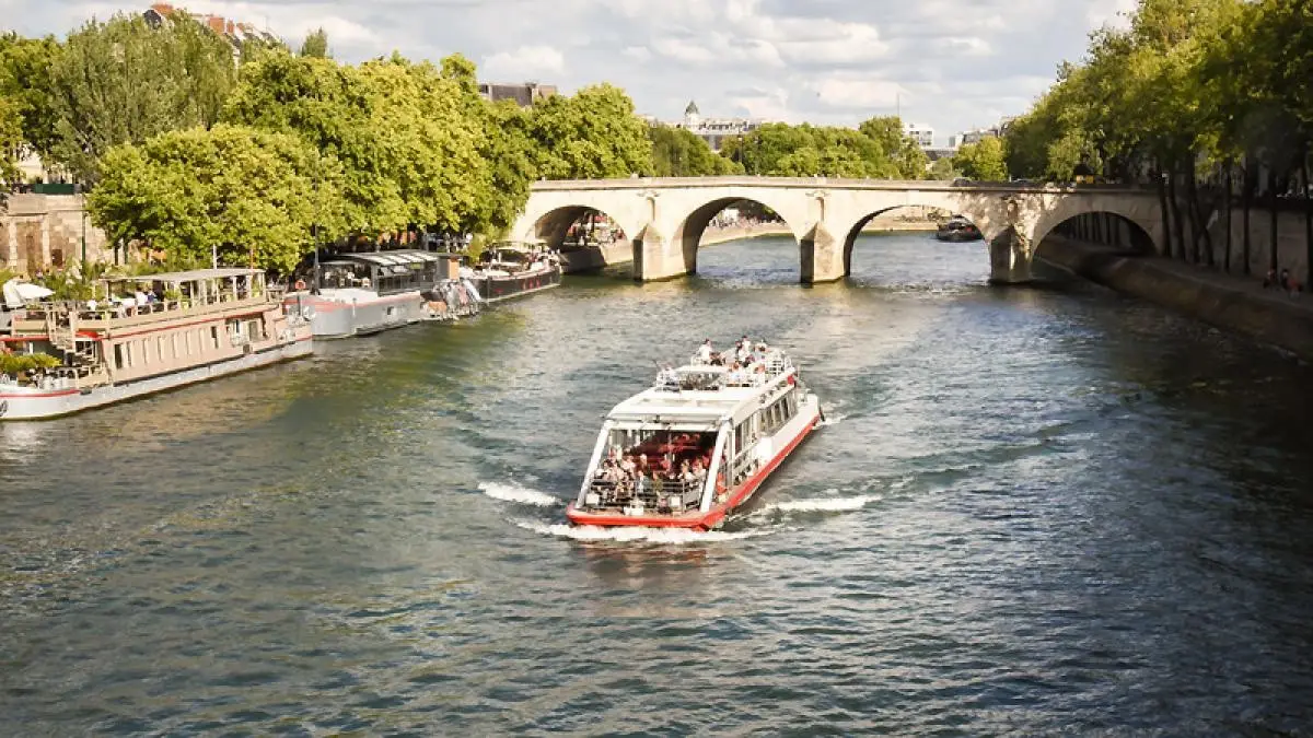 A canal sightseeing boat in Paris glides through the Seine River near shaded riverbanks and footbridges. A canal sightseeing boat in Paris glides through the Seine River near shaded riverbanks and footbridges.