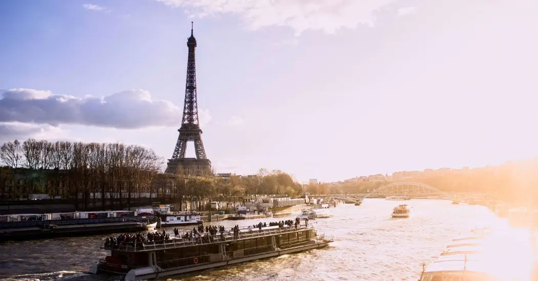 Tour boat sails near Eiffel Tower in Paris afternoon glow.
