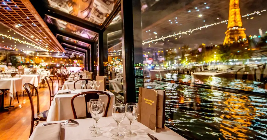 Eiffel Tower sparkles beside glass-enclosed Seine dinner cruise.