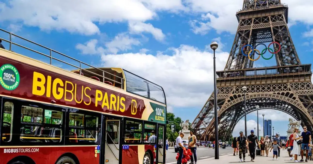 Tourists boarding a hop-on hop-off bus beside the Eiffel Tower in Paris.
