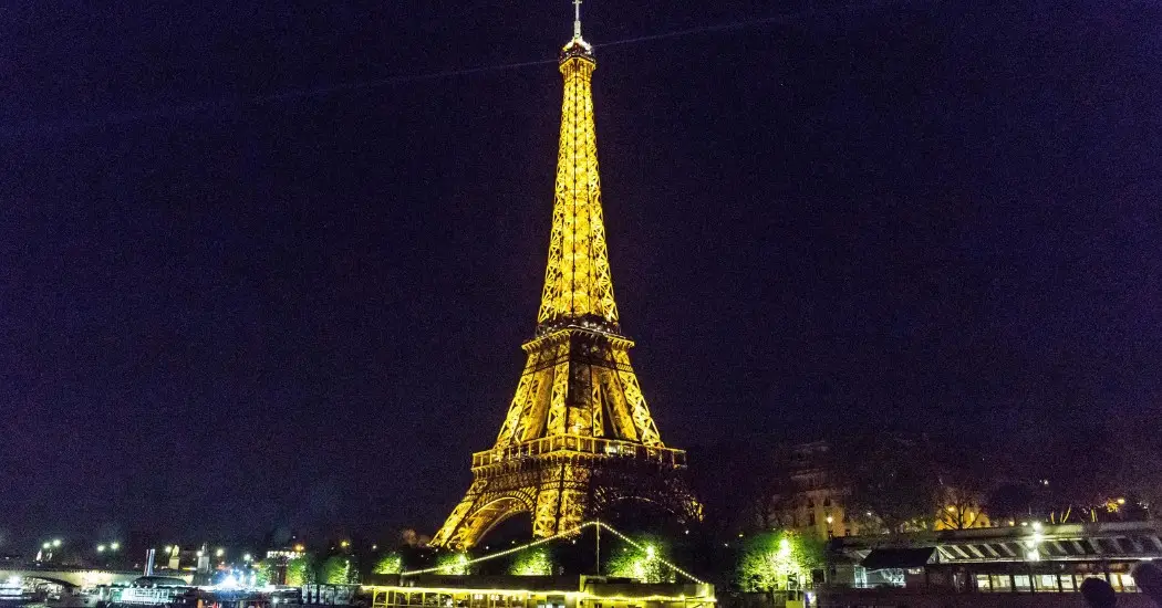 Eiffel Tower glowing at night with Seine cruise boats below.