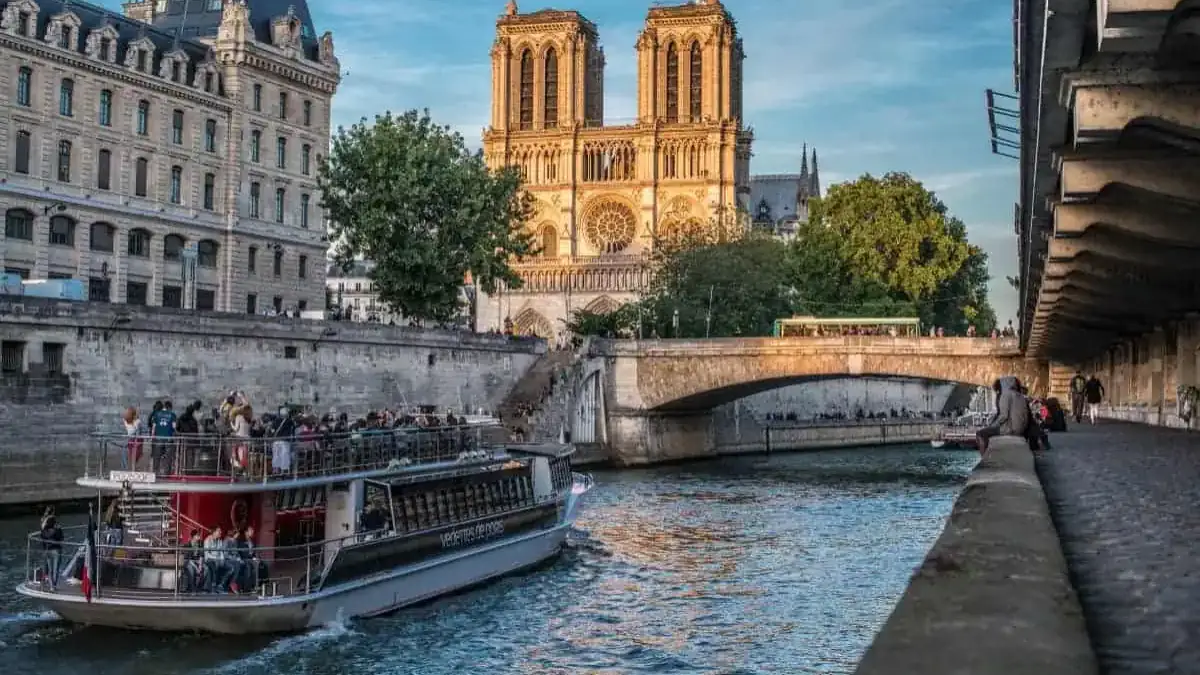 notre-dame-seine-cruise-paris Seine River cruise boat passing Notre-Dame Cathedral at sunset in Paris, France