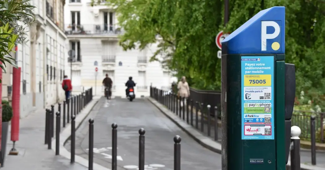 Public parking machine on quiet Paris street with traffic bollards.