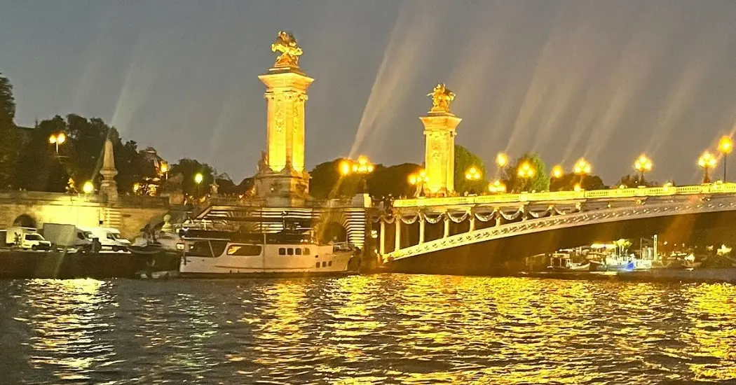 Nighttime Seine River sparkles below ornate Pont Alexandre III bridge.
