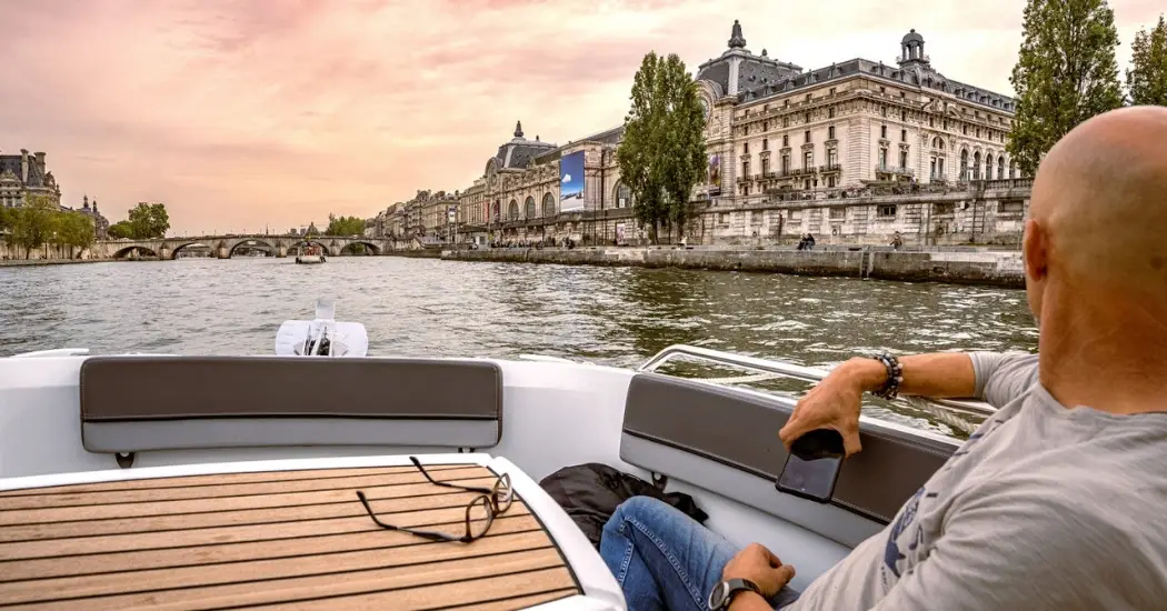 A man enjoys a private Seine River cruise in Paris while viewing the Musée d'Orsay at sunset.
