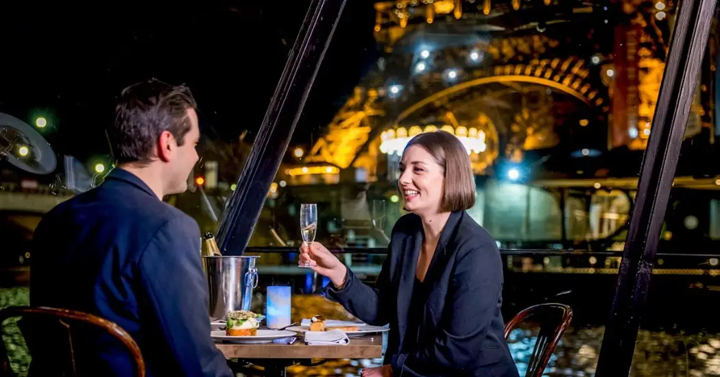 Smiling couple toasting champagne aboard a Paris evening cruise.