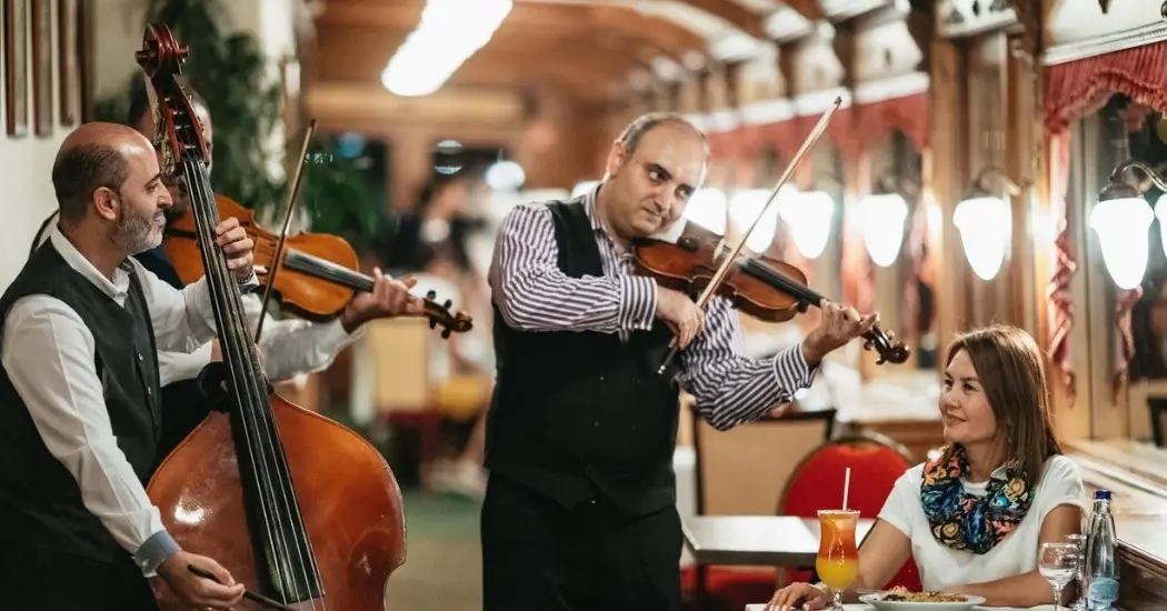 A Trio of musicians performs live beside a woman enjoying dinner.
