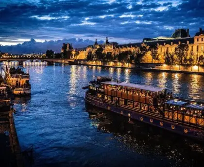 Seine River dinner cruise boat illuminated at night with glowing Paris landmarks in the background