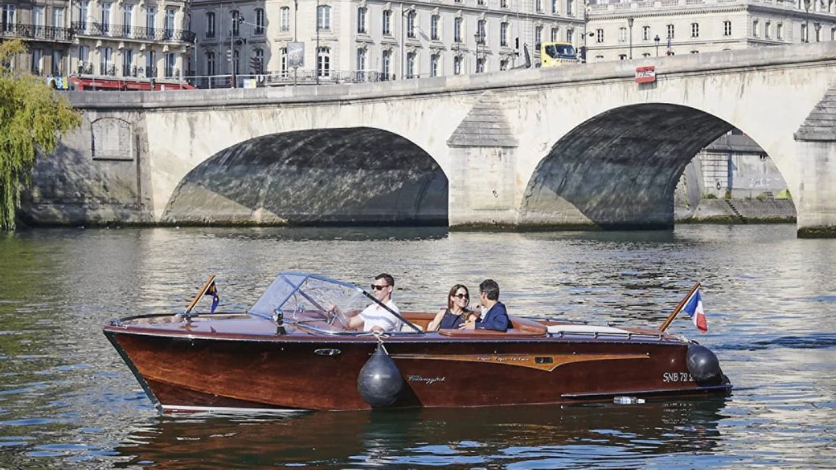 A small luxury boat cruising on the Seine River near a historic Paris bridge.